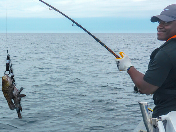 A person holds a fishing pole with two fish on the end while standing on a boat.